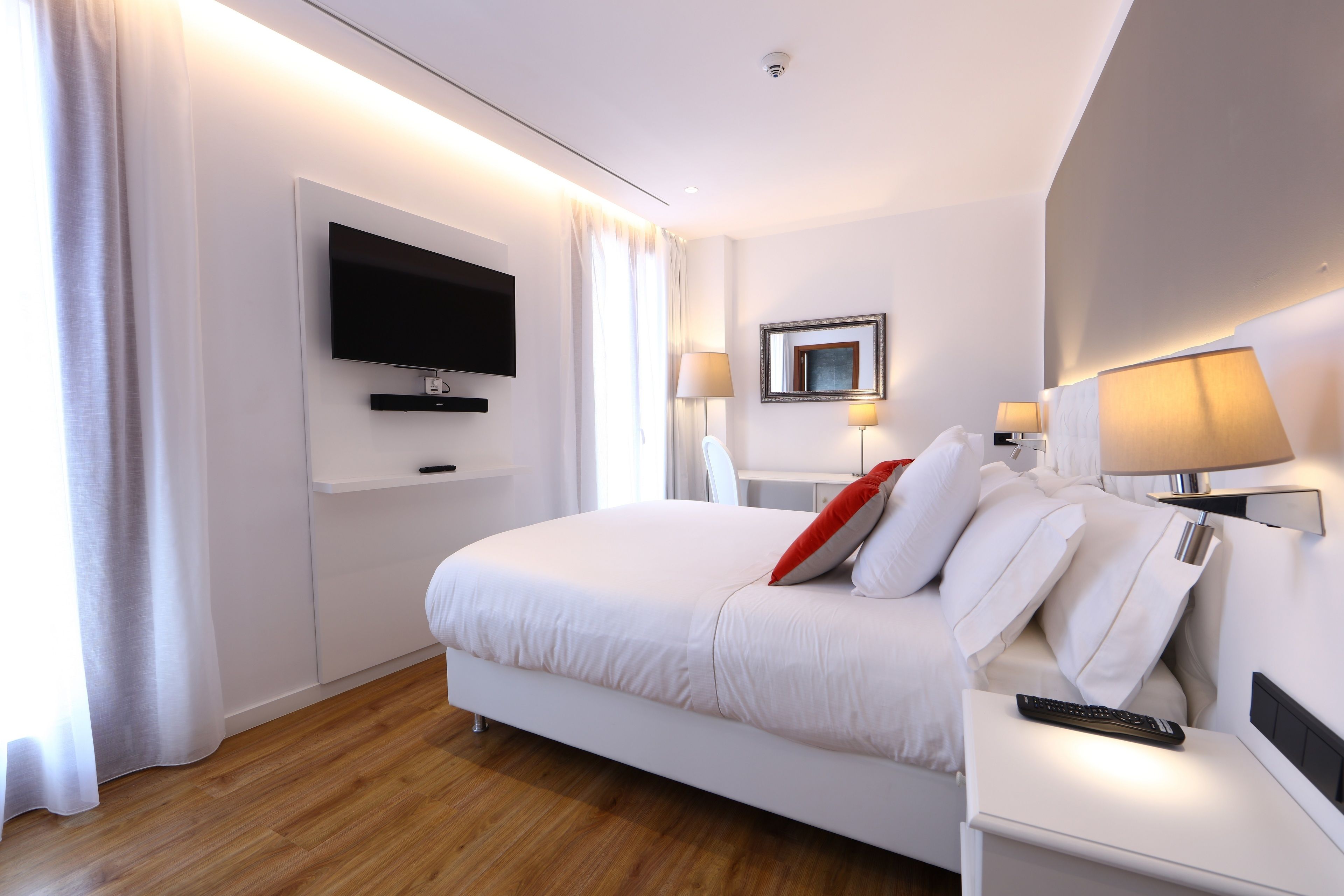 Habitación de hotel moderna con una cama grande, un televisor de pantalla plana montado en la pared, lámparas de noche y una mesita de noche.