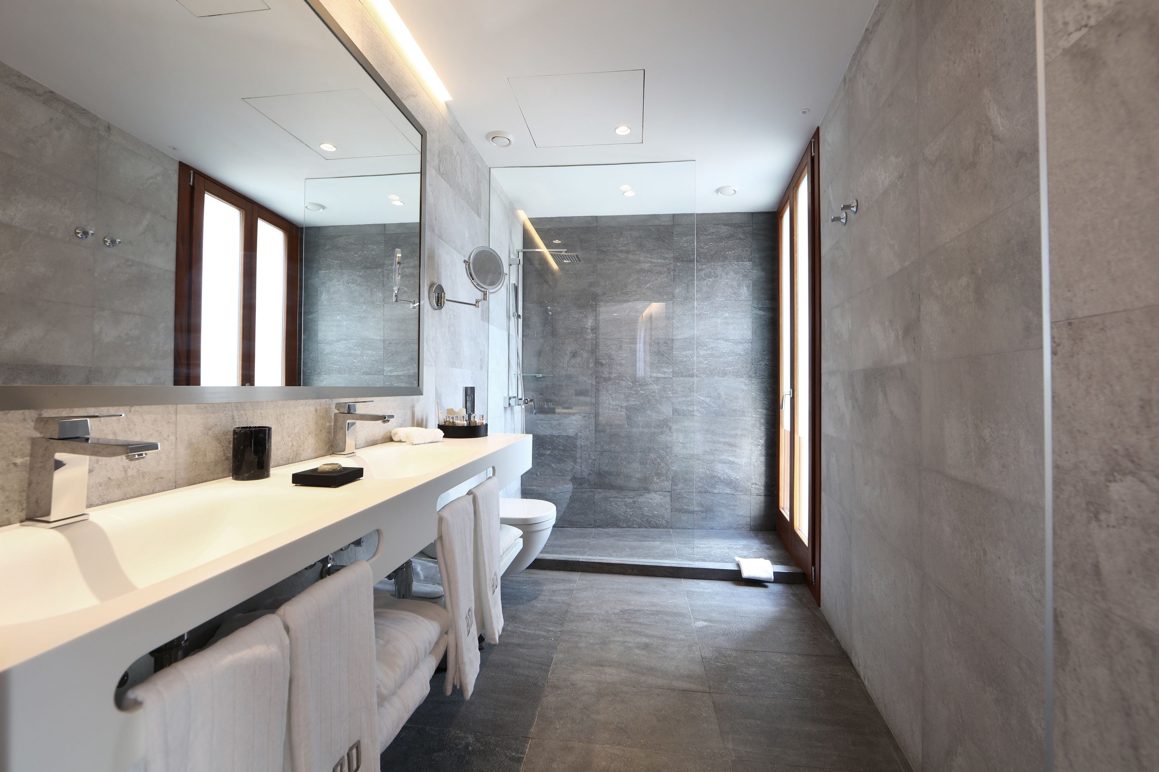 Un baño moderno con un espejo grande, dos lavamanos, una ducha y una zona de ducha a ras de suelo.