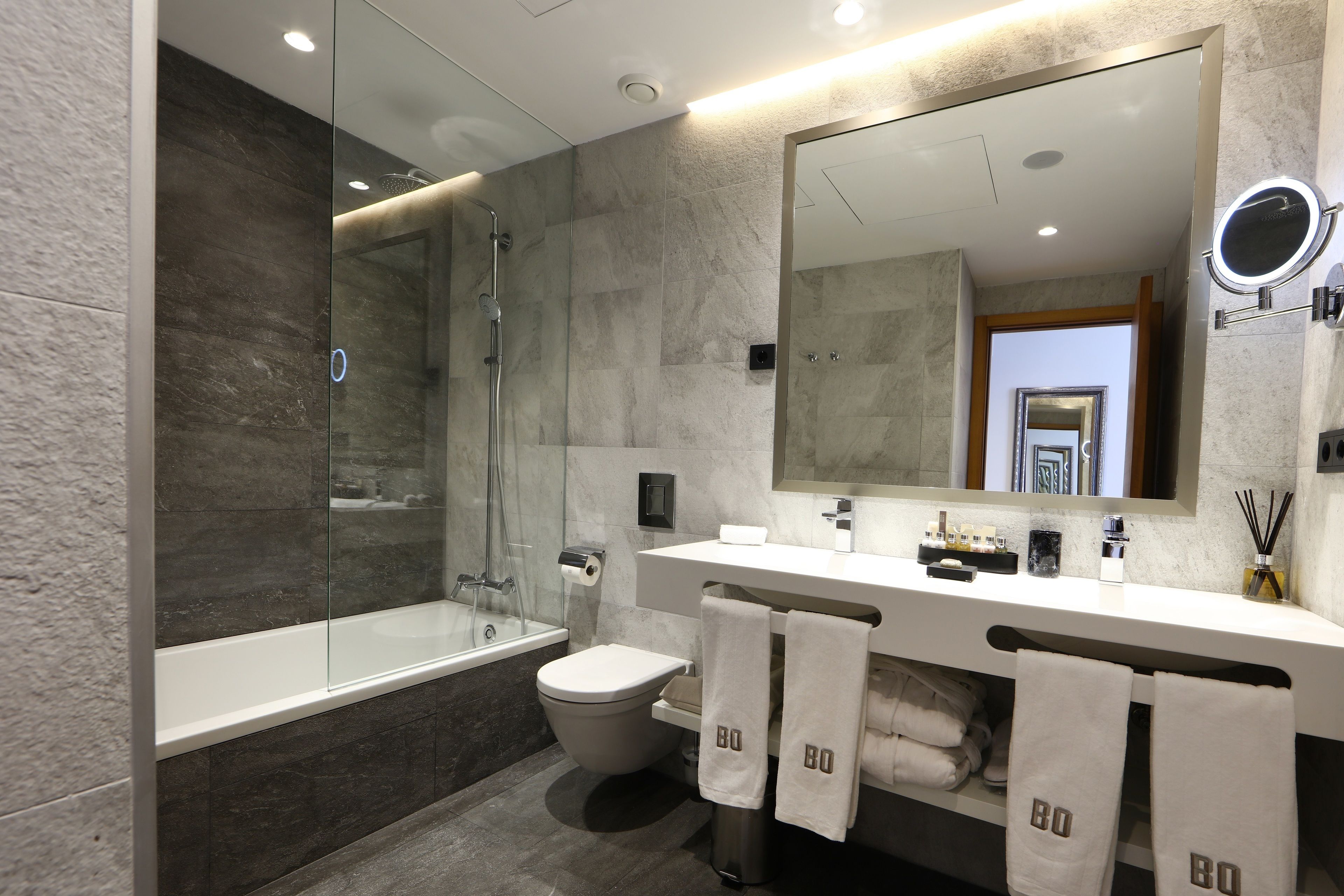 Un baño moderno con ducha de vidrio, bañera, inodoro y tocador con un espejo grande.