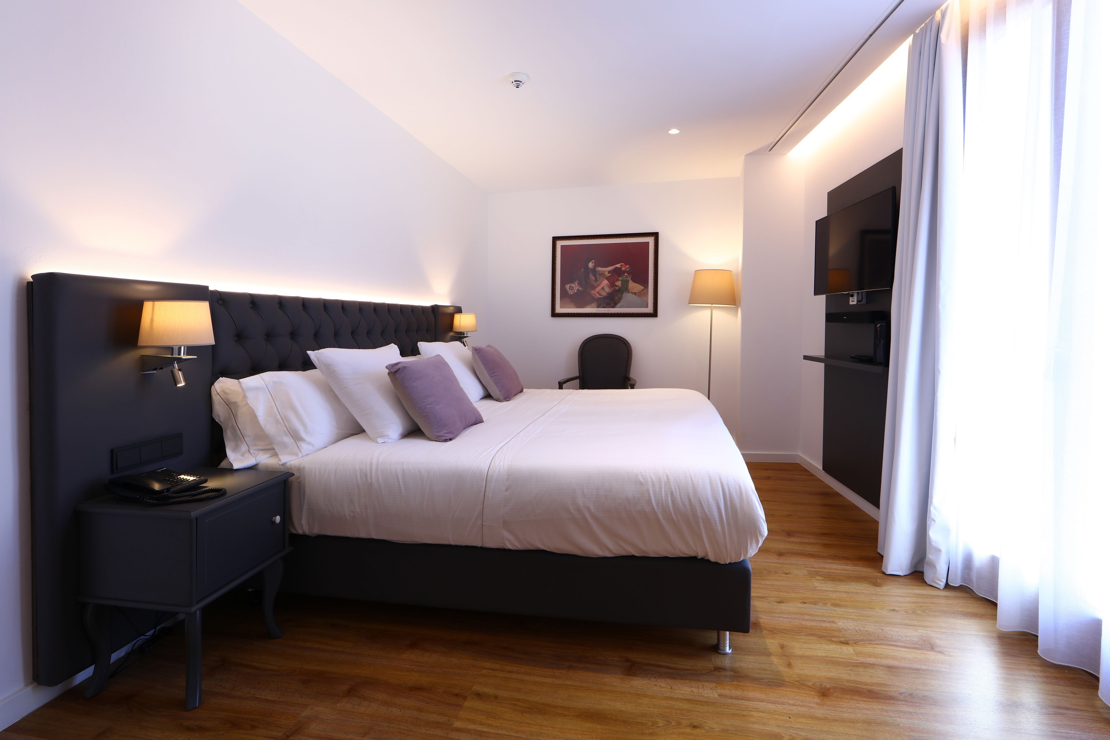 A modern hotel room with a large bed, bedside tables, a flat-screen TV, and a painting on the wall.