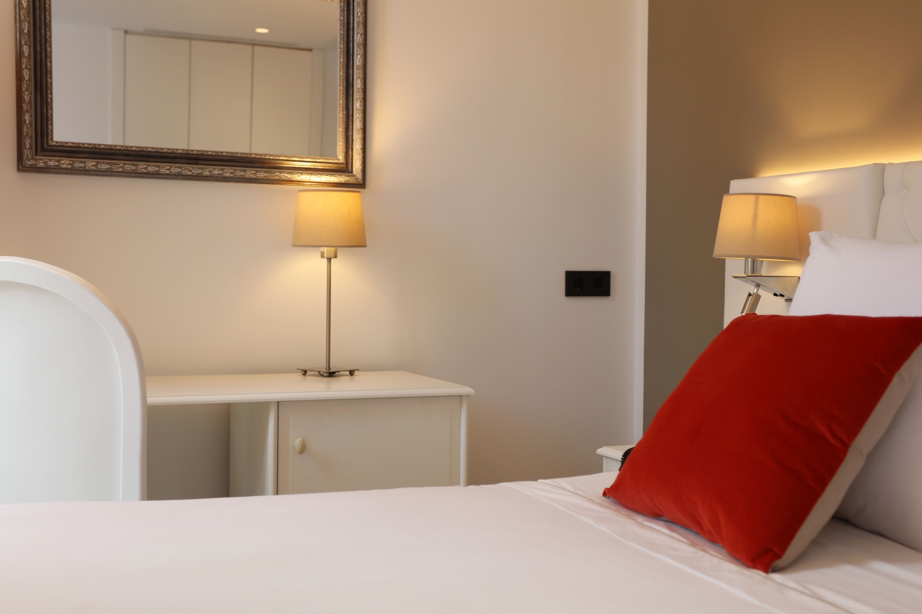 A hotel room with a bed, bedside tables, lamps, and a mirror.