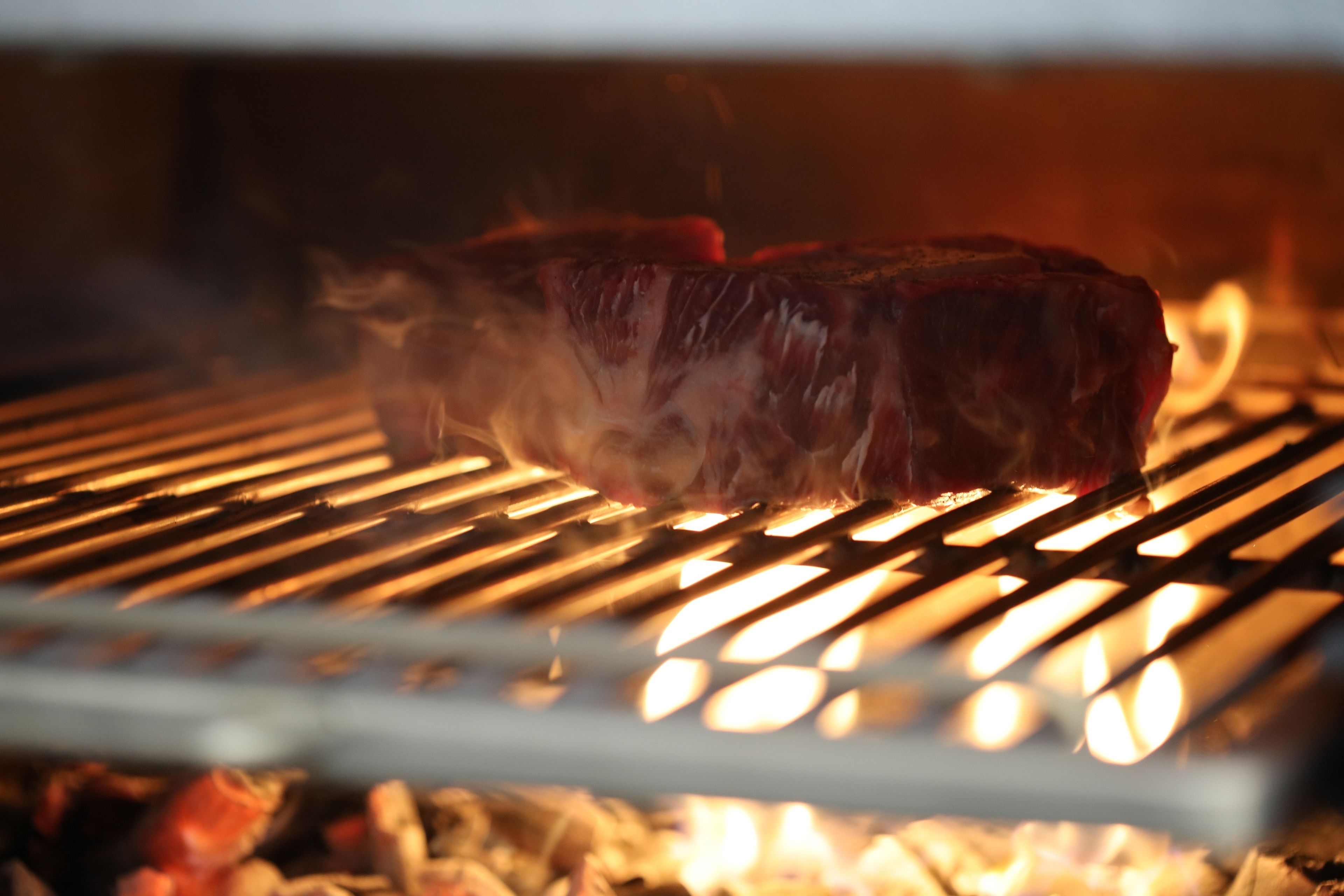 Ein Steak wird auf einem Grill mit sichtbaren Flammen zubereitet.