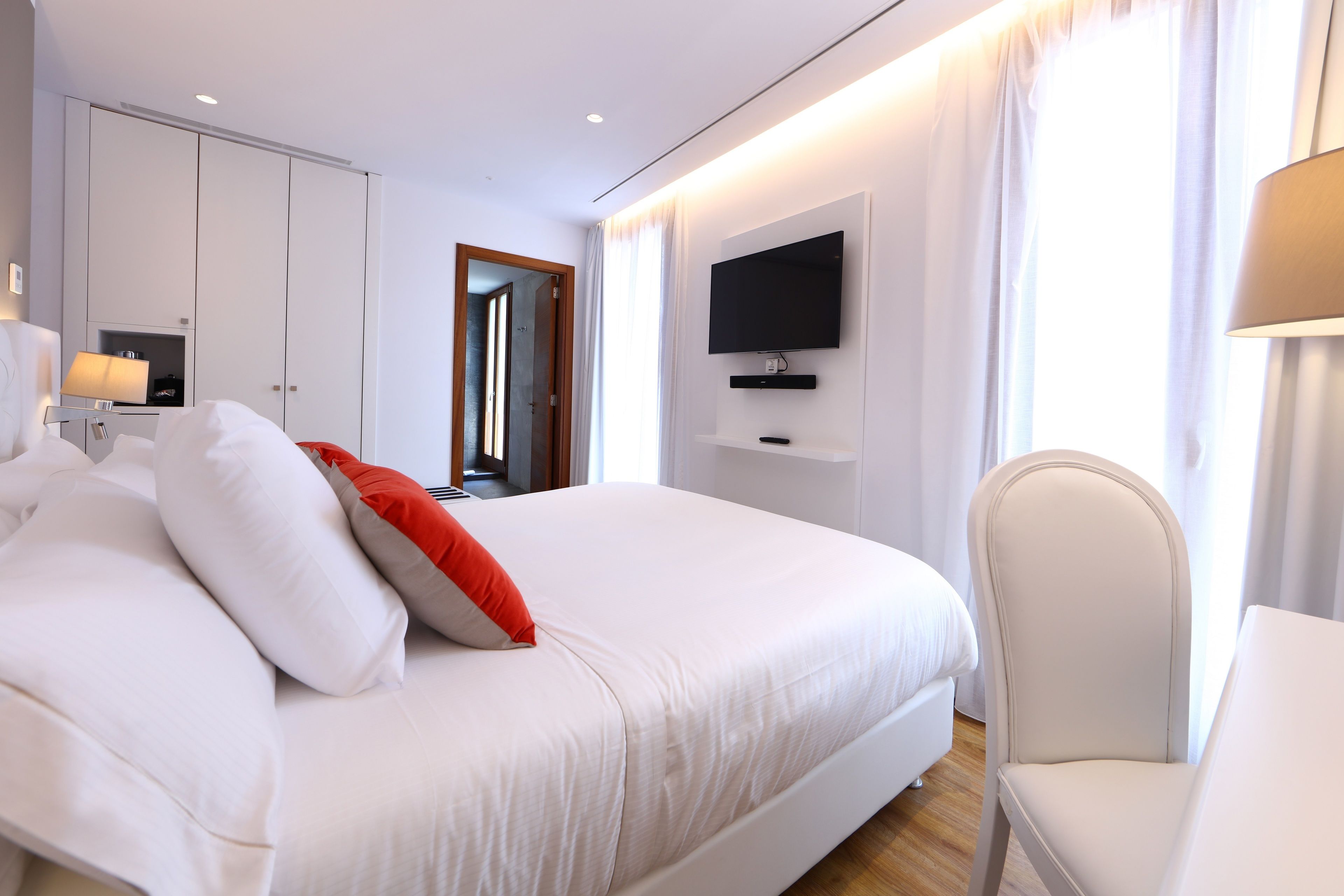 Una habitación de hotel moderna con una cama grande, un televisor montado en la pared y un escritorio con una lámpara.