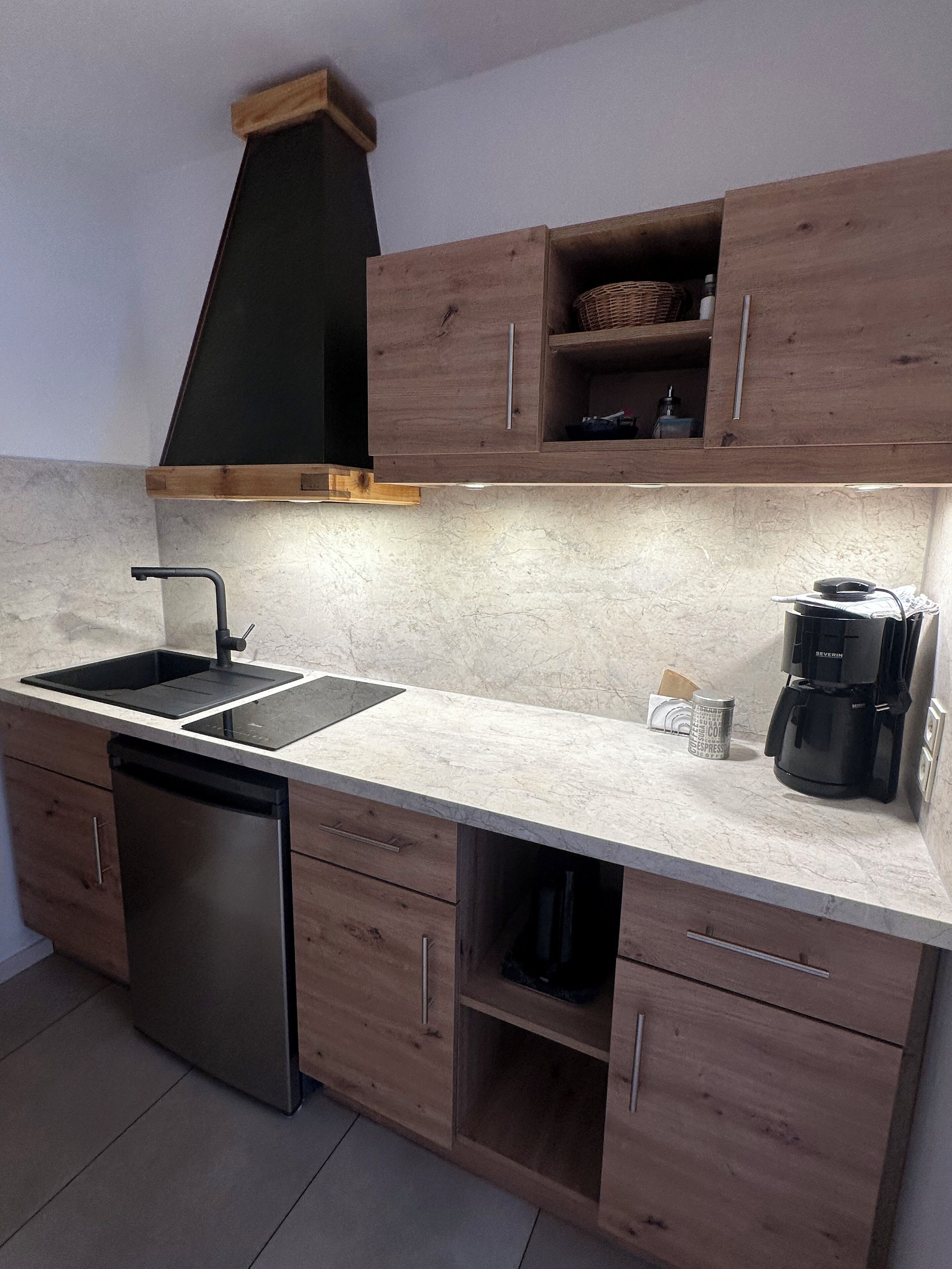 Una cocina compacta con lavavajillas, un lavamanos, cafetera y armarios de madera.
