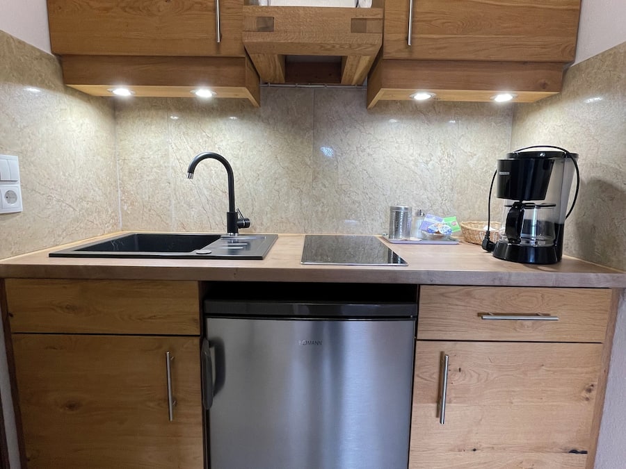 A compact kitchen with wooden cabinets, a stainless steel dishwasher, a black coffee maker, and a marble backsplash.