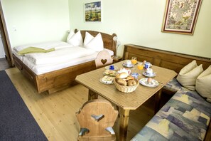 A cozy room with a bed, a wooden table with breakfast items, a chair, and a sofa. - Gästehaus Gastl (Mieming)