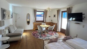 Ett modernt, väl upplyst rum med en säng, en soffa, ett matbord med stolar, en tv och ett stort fönster.