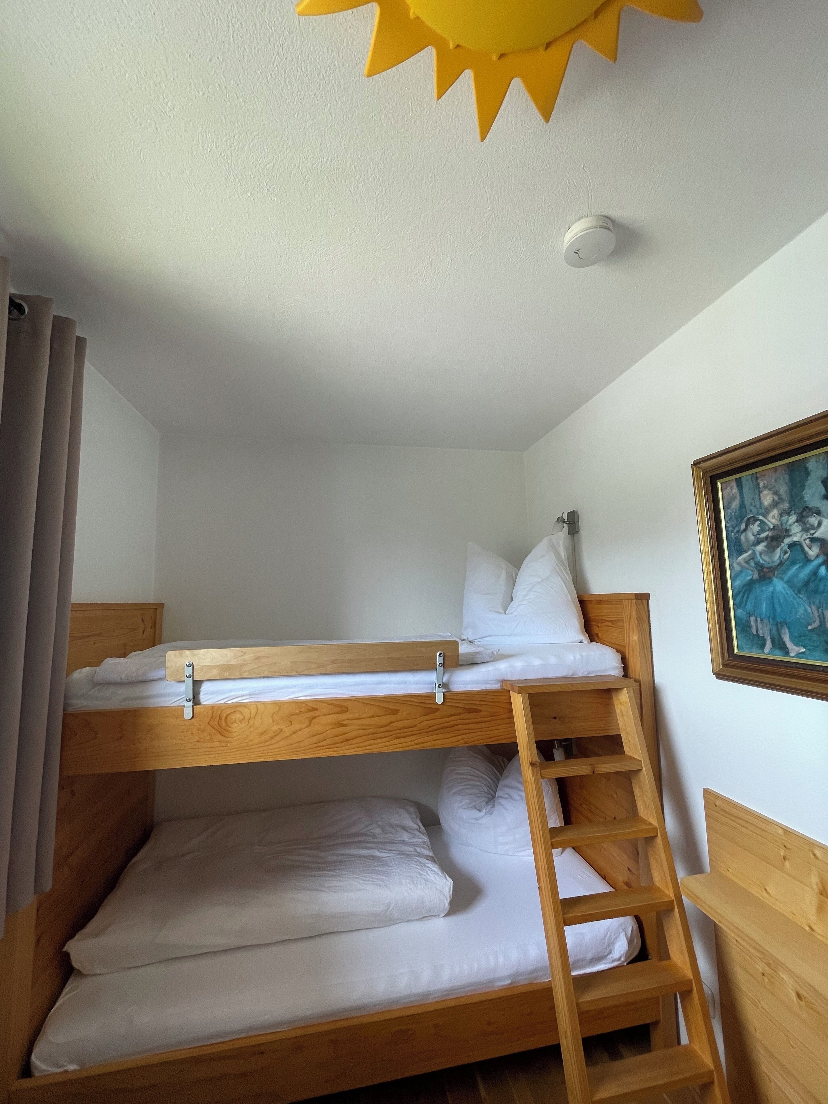 Een slaapkamer met een stapelbed, een houten ladder, wit beddengoed en een plafondlamp.