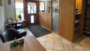 Ett rum med en receptionsdisk i trä, en matplats med stolar och ett bord, ett klinkergolv och en bokhylla.