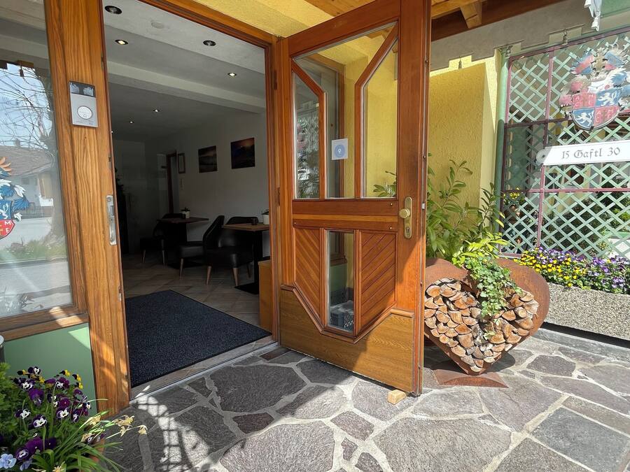 A wooden door leading into a room with a stone floor, a potted plant, and a heart-shaped planter with logs.