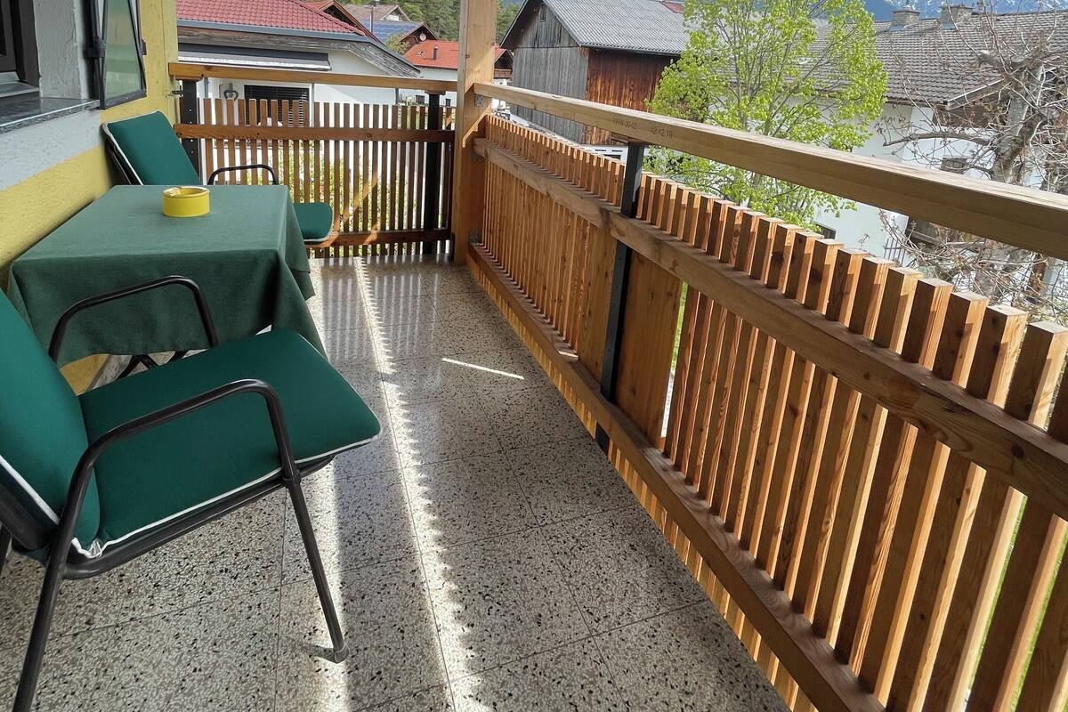 A balcony with a view of snow-capped mountains, wooden railings, and a table with chairs.
