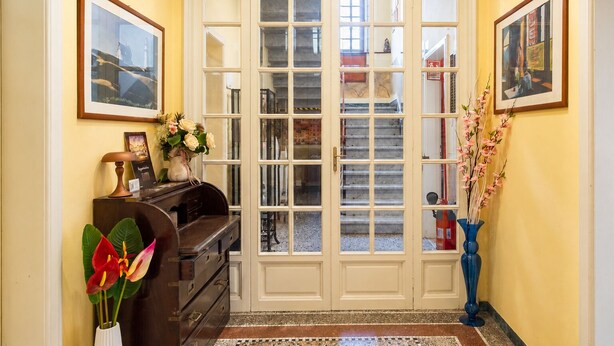 A hallway with a double door, a desk with a lamp, a vase with flowers, and a blue vase with branches. - Villa Catelli B&B (Lucca)