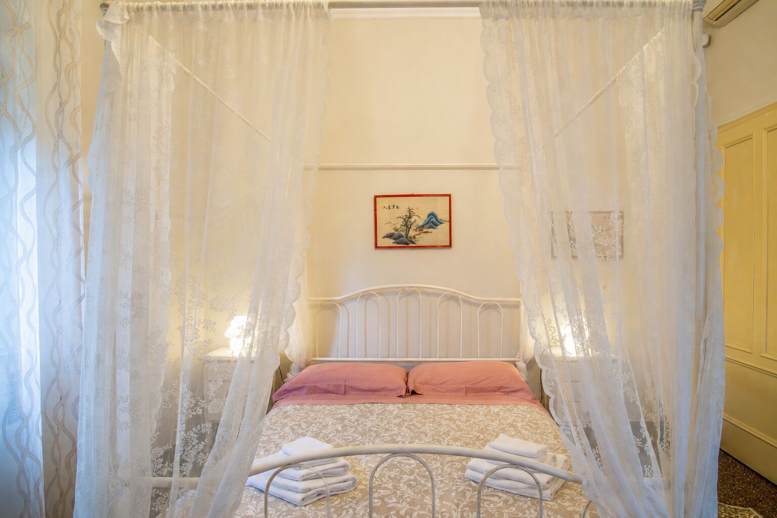 Ein Bett mit Baldachin, ein gerahmtes Bild an der Wand und ein weißer Metallbettrahmen.