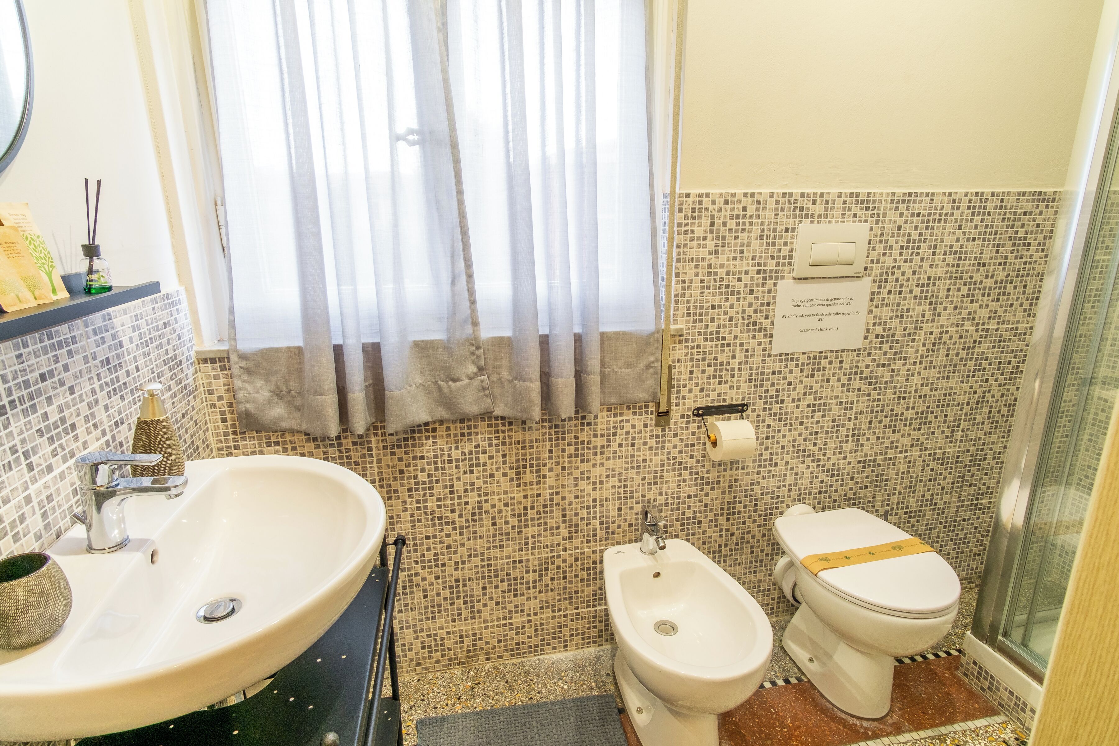 A bathroom with a sink, bidet, and toilet, tiled walls, and a shower area.