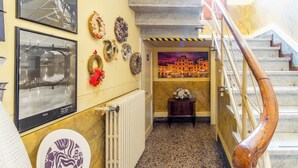 A hallway with a staircase, framed photographs on the walls, and a radiator. - Villa Catelli B&B (Lucca)