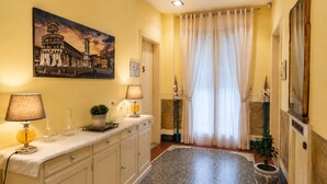 A hallway with a marble floor, a painting of a historical building, a lamp, and a potted plant. - Villa Catelli B&B (Lucca)