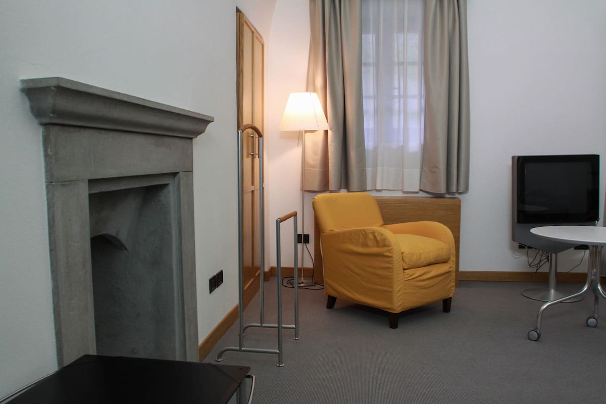 A hotel room with a fireplace, a lamp, a yellow armchair, a television, and a small table.
