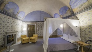 Una habitación con cama con dosel, televisión, dos sillones amarillos y chimenea.