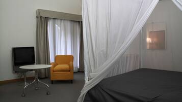 A hotel room with a bed, a television, a small table, an armchair, and a window with curtains.