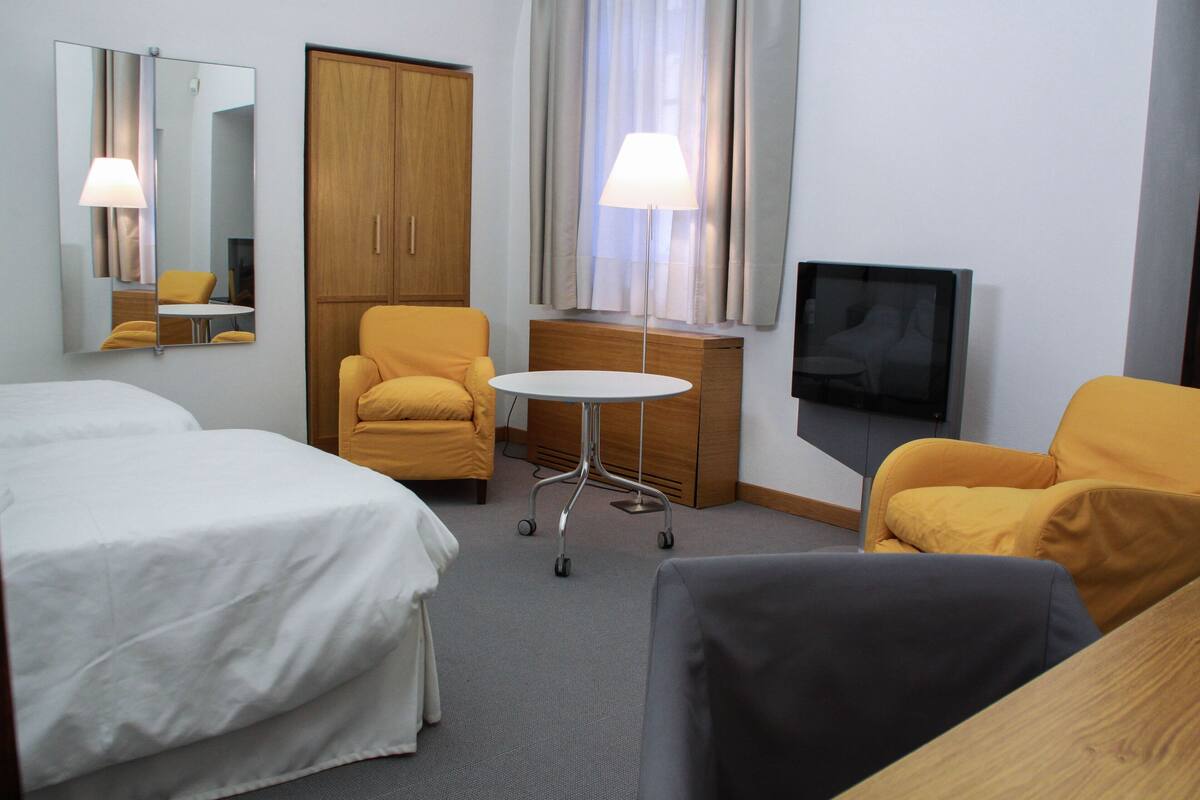A hotel room with two beds, a desk, a chair, a television, and a lamp.