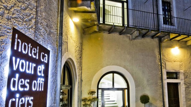 Entrada de un hotel con un letrero que dice 'hotel ca votre et des officiers' y un patio empedrado de piedra.