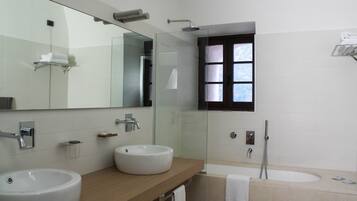 A modern bathroom with two sinks, a large mirror, a glass-enclosed shower, and a window with blinds.