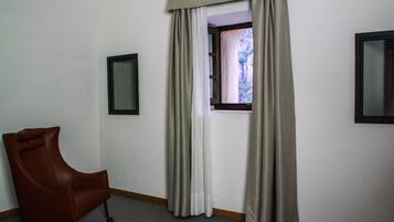 A room with a single brown leather chair, a window with beige curtains, and two framed pictures on the walls.