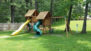 A wooden play structure with a slide and swings in a grassy park area. - Seabrook Inn (Seabrook)