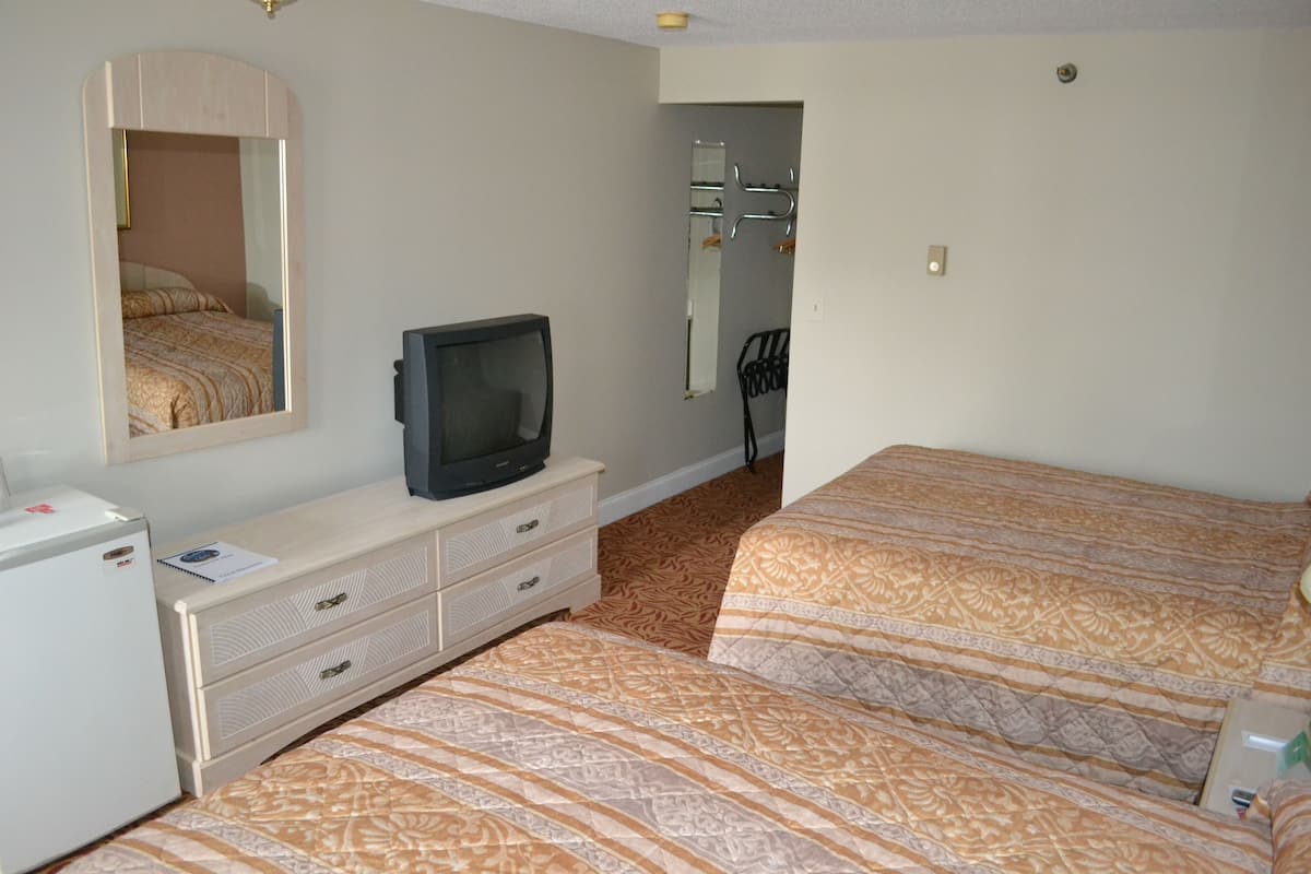 A hotel room with two beds, a television, a dresser, and a mirror.