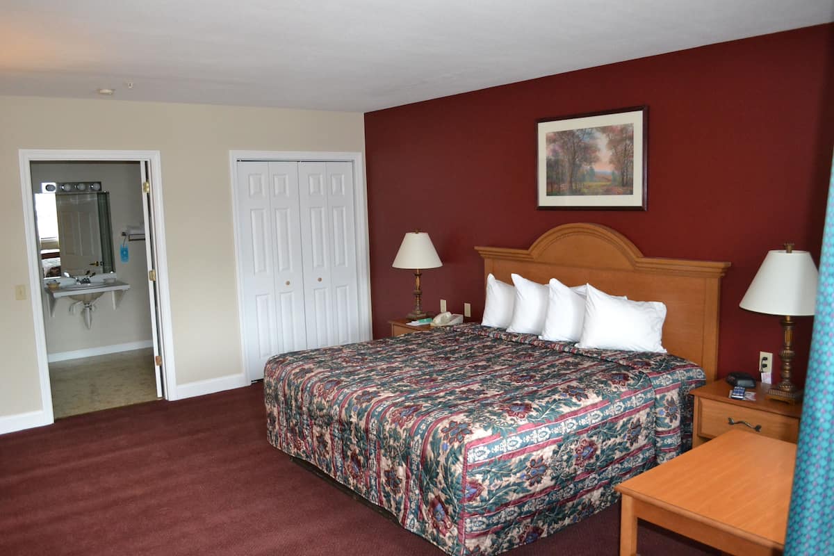 A hotel room with a large bed, two bedside lamps, a wooden nightstand, and a painting on the wall.