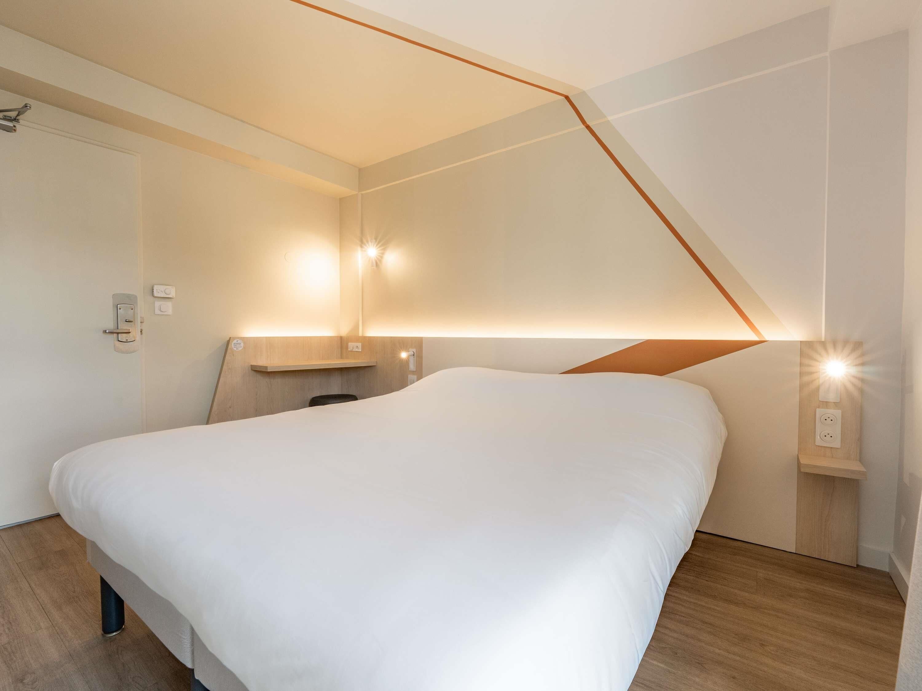 Una habitación de hotel moderna con una cama grande, un cabecero de madera e iluminación empotrada en la pared.