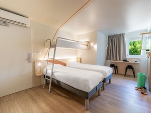 Une chambre d’hôtel compacte comprenant deux lits superposés, un bureau, une chaise, une fenêtre avec vue et un ballon d’exercice vert.