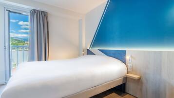 Une chambre d’hôtel moderne dotée d’un grand lit, offrant une vue sur l’extérieur et agrémentée d’un mur d’accent d’une couleur bleue originale.
