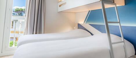 A room with two bunk beds, a window with curtains, a balcony, and a blue accent wall.