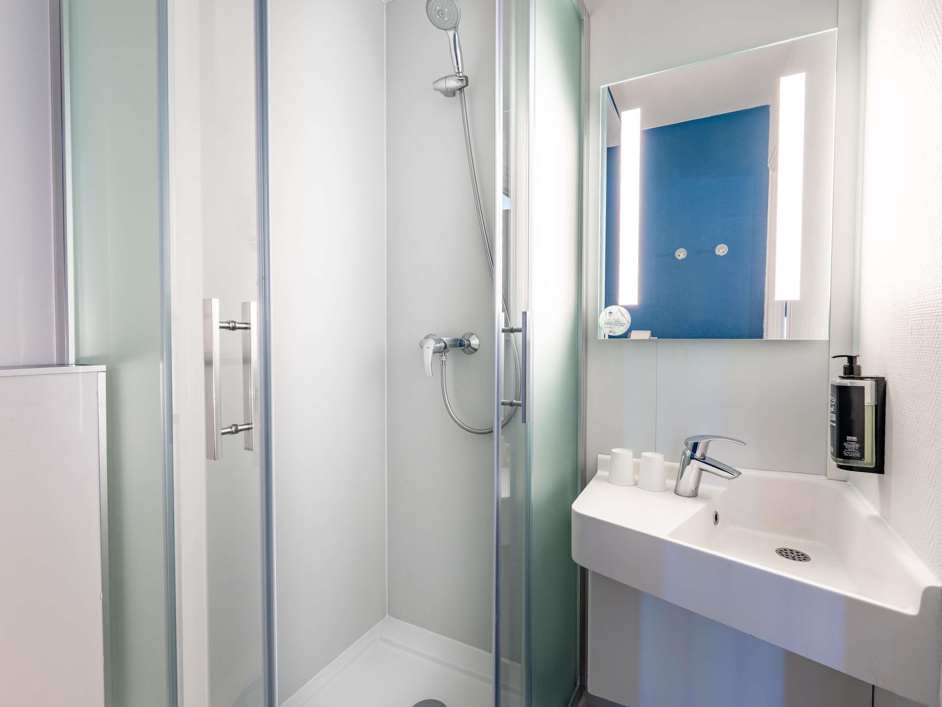 A modern bathroom with a glass shower enclosure, a white sink, and a mirror with a blue accent wall.