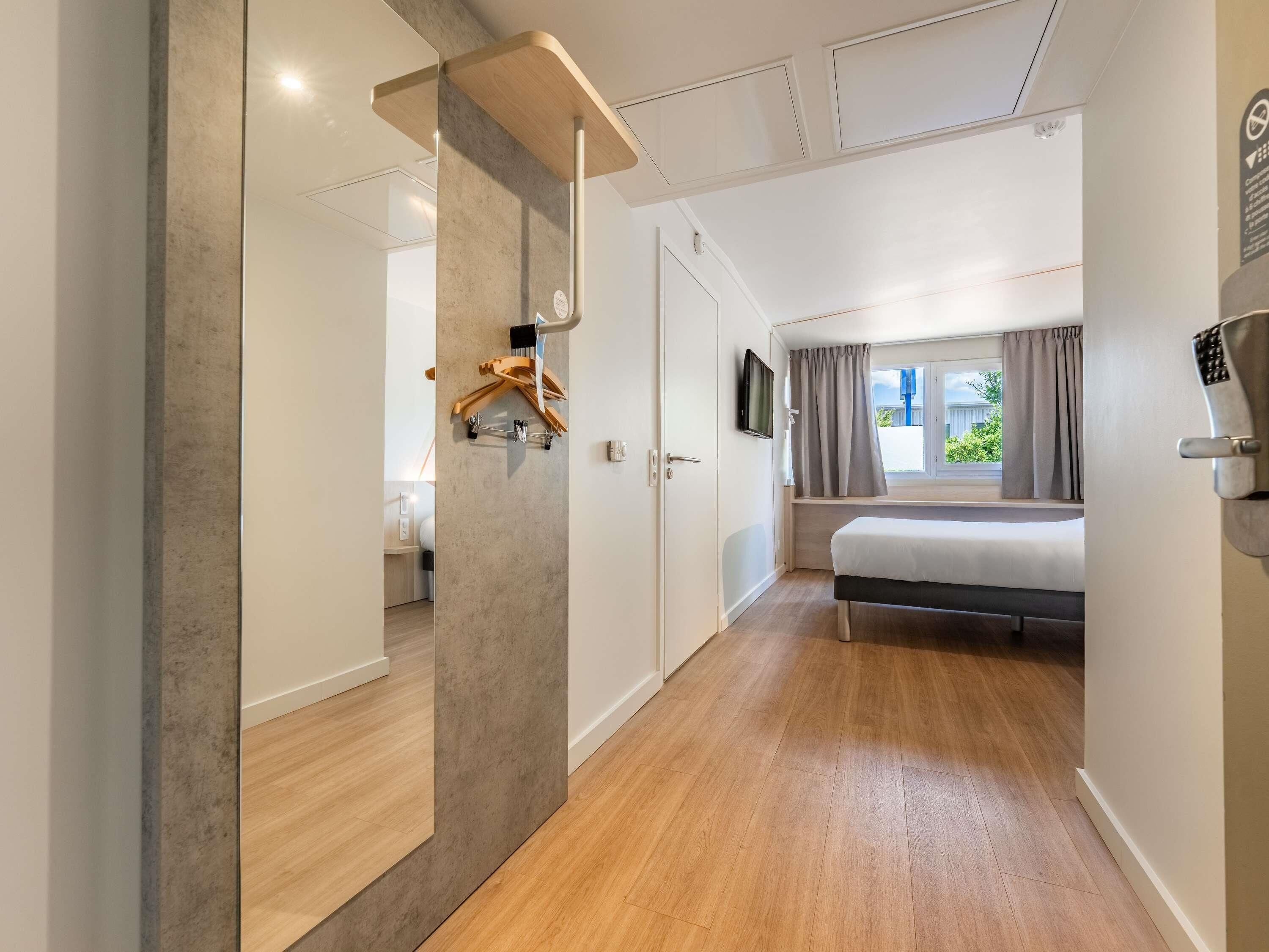 Une chambre d’hôtel moderne avec un plancher en bois, un lit, une télévision et une fenêtre avec des rideaux.