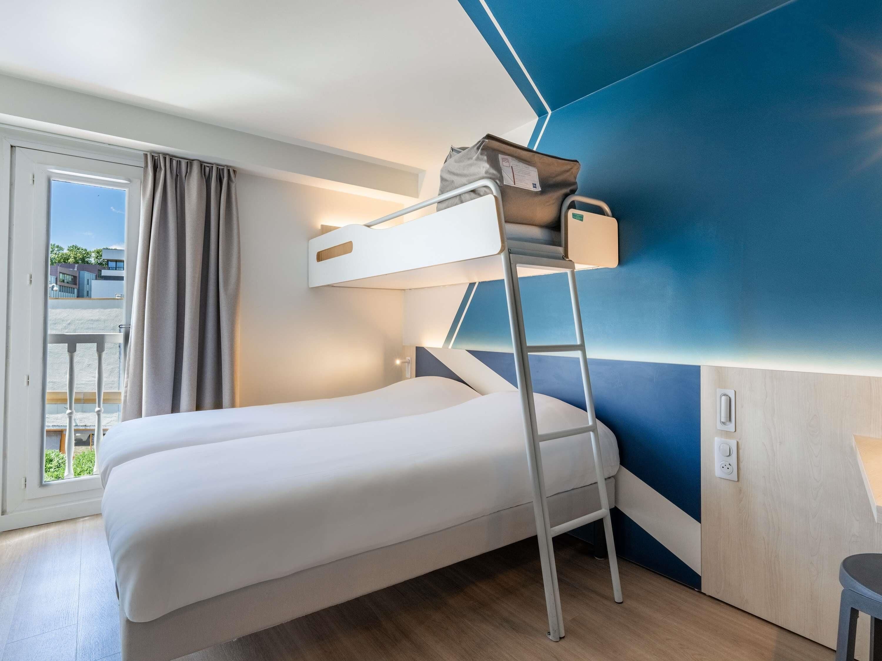 Un lit superposé avec une échelle, une fenêtre avec des rideaux et une vue sur la verdure à l’extérieur.