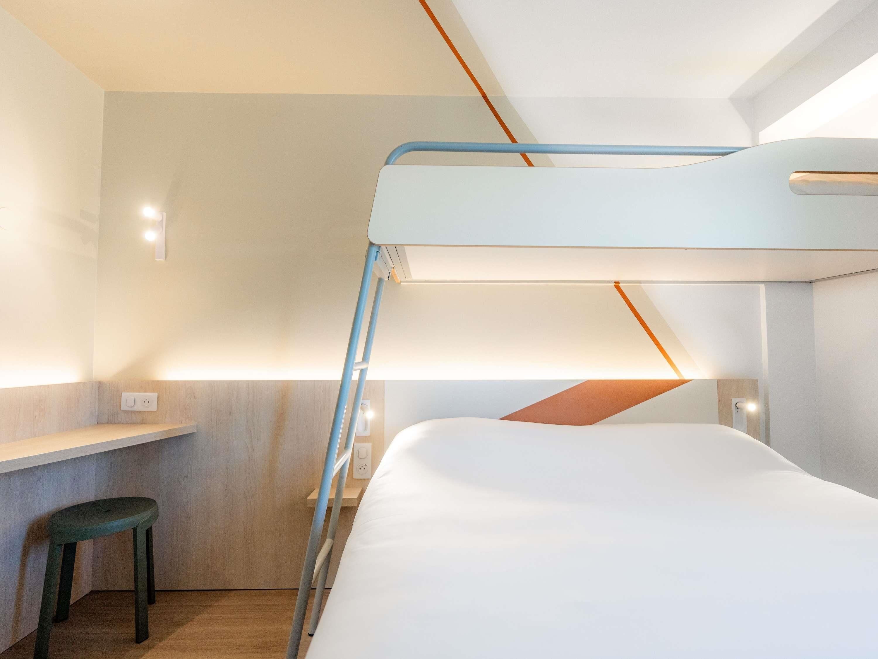 Ein Stockbett mit Schreibtisch und Hocker in einem modernen Zimmer mit Holzboden und indirekter Beleuchtung.