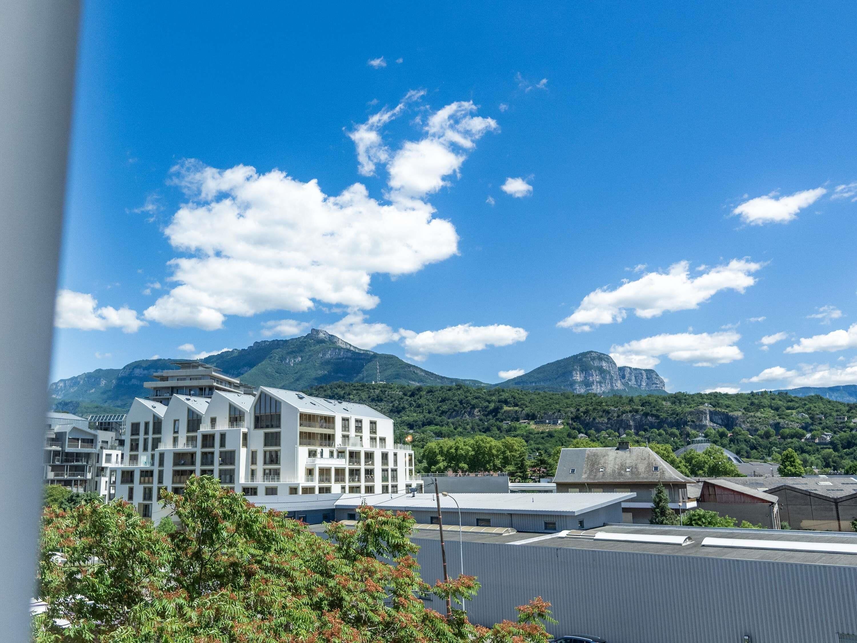 Un bâtiment moderne doté d’un toit plat, entouré de verdure et avec des montagnes en toile de fond.