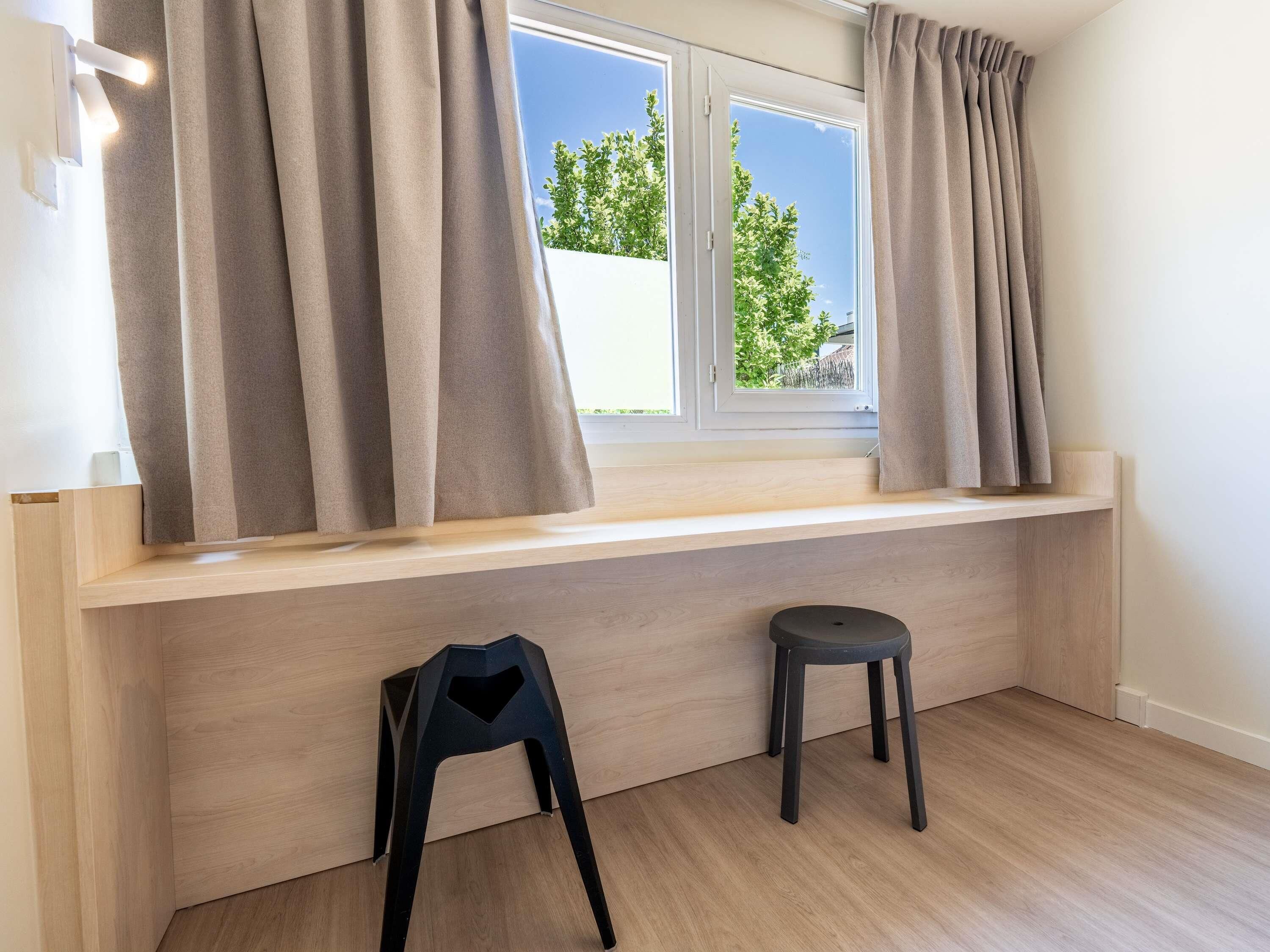 A room with a window, a wooden bench, and two stools.