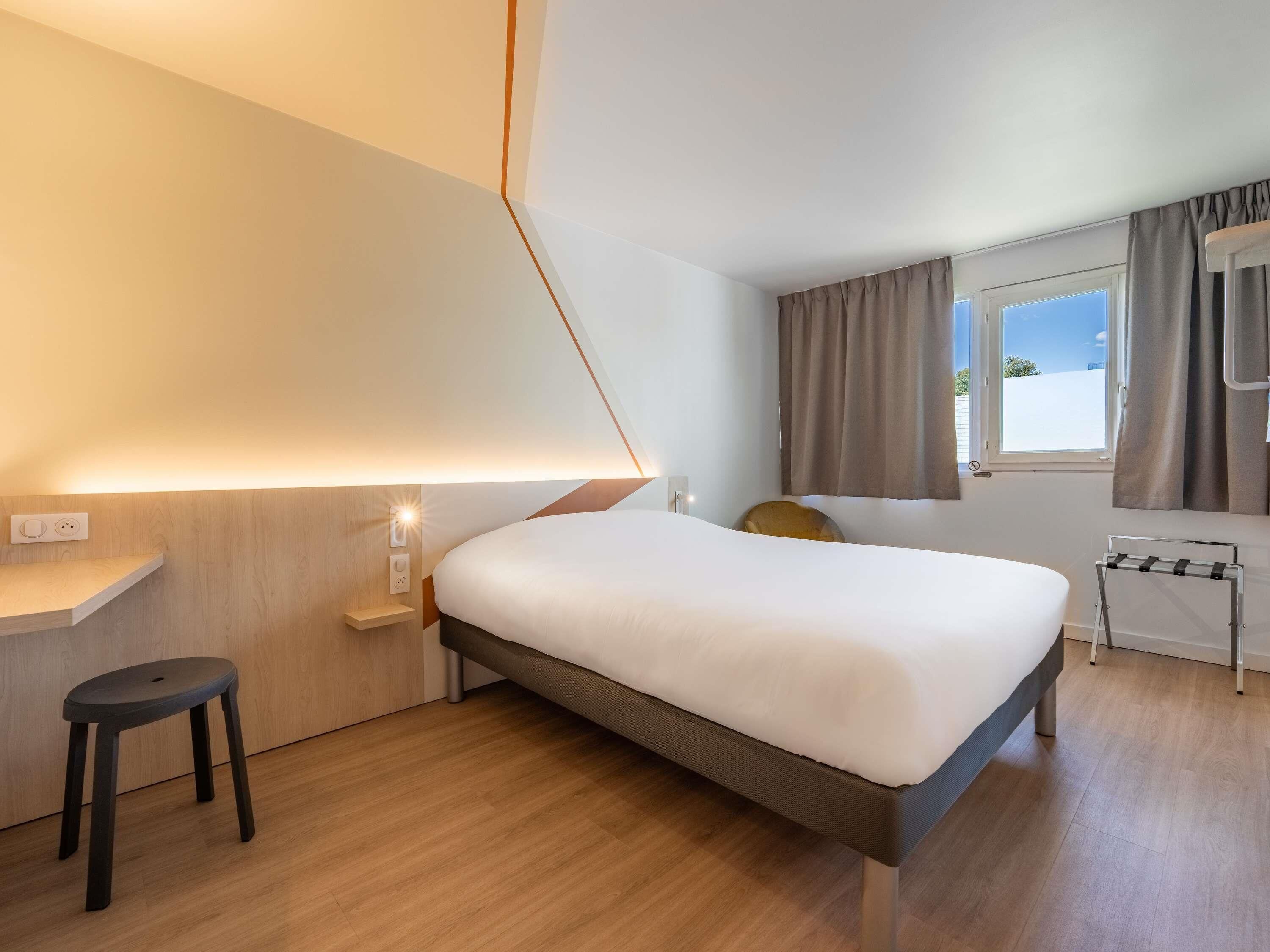 Una habitación de hotel moderna con cama, escritorio, silla y ventana con cortinas.