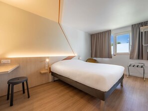 Quarto de hotel moderno com cama, escrivaninha, cadeira e janela com cortinas.