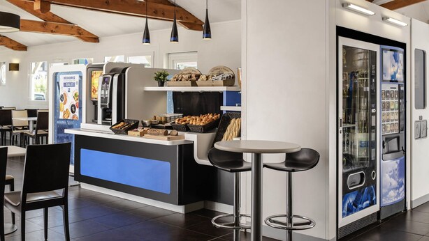 Ein modernes Café mit einer zentralen Theke, Barhocker, einer Kaffeemaschine und einer Kühlvitrine.