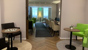 A modern hotel room with a dining area, a sofa, and a table with a chessboard.