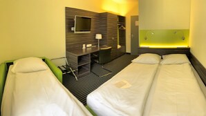A hotel room with two single beds, a desk with a chair, a small seating area, and a shower area.