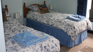 A room with two beds, each with a wooden headboard, a blue and white floral bedspread, and a blue blanket on one bed. - The Old School House (Llanbrynmair)
