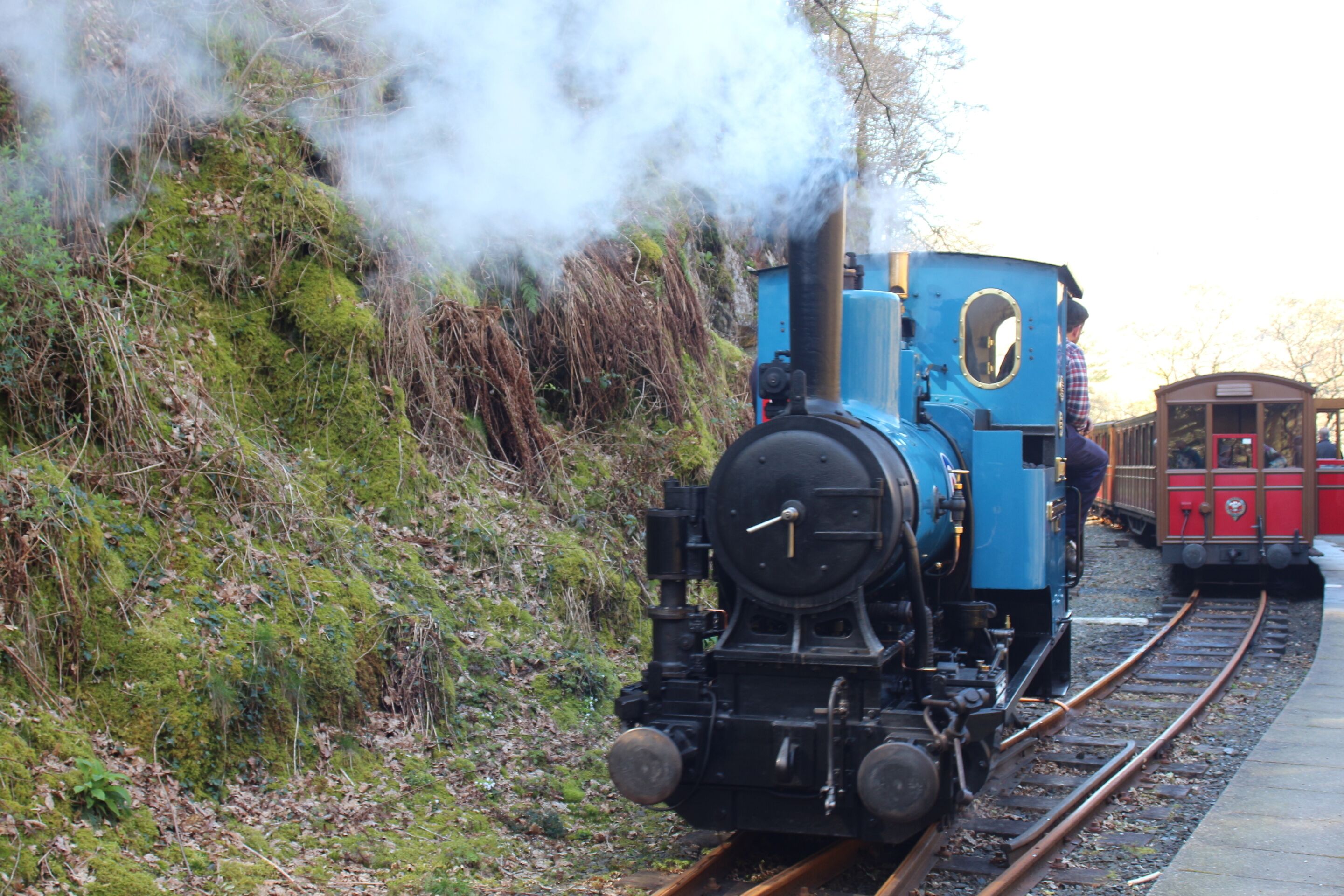 Une locomotive à vapeur sur des rails, avec un wagon de voyageurs rouge.