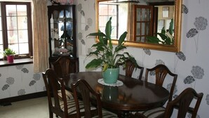 A dining room with a round wooden table surrounded by six chairs, a potted plant on the table, and a large mirror on the wall. - The Old School House (Llanbrynmair)