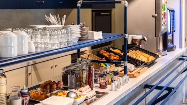 A buffet setup with various food items, condiments, and utensils. - ibis budget Lyon Villefranche sur Saône (Limas)
