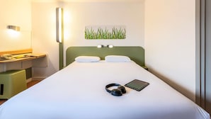 A hotel room with a bed, bedside table, lamp, and a wall-mounted artwork of grass. - ibis budget Lyon Villefranche sur Saône (Limas)